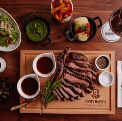 Savour succulent steak with sides at Fibber McGee's Steakhouse; dine in style with fresh salad and wine on a wooden table.