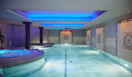 Luxurious indoor pool with serene blue lighting and mosaic decor, featuring adjacent whirlpool spa. Relaxation awaits.