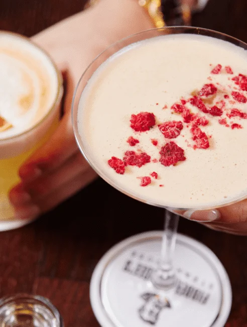 Two crafted cocktails on coasters at a hotel bar — creamy martini with crushed raspberries and citrus foam cocktail, ideal for relaxed evening dining